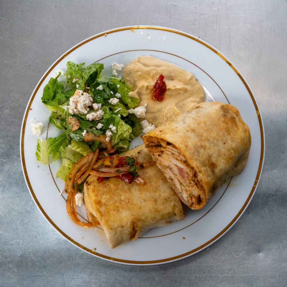 Plate of stuffed flatbread with chicken, roasted vegetables, green salad, feta cheese, and red pepper sauce.